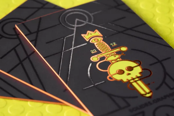 A black business card with glossy spot UV geometric linework catching the light and copper foil edges.