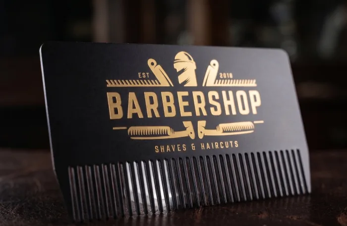 A black die-cut "Barbershop" metal card shaped like a hair comb, with gold-foiled logo and lettering.