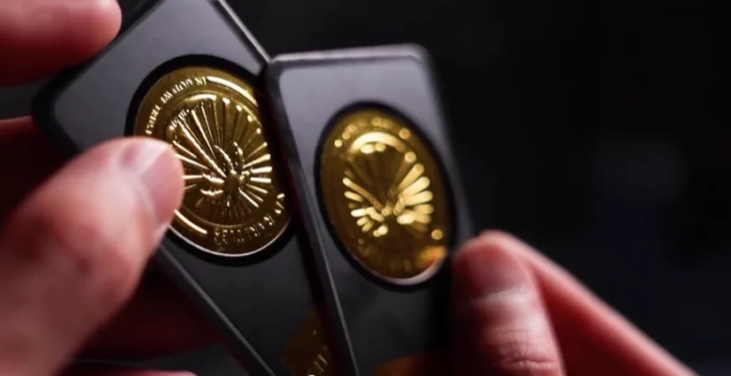 Two black business cards fanned open, each with a large raised gold foil coin emblem lifted well off the surface.